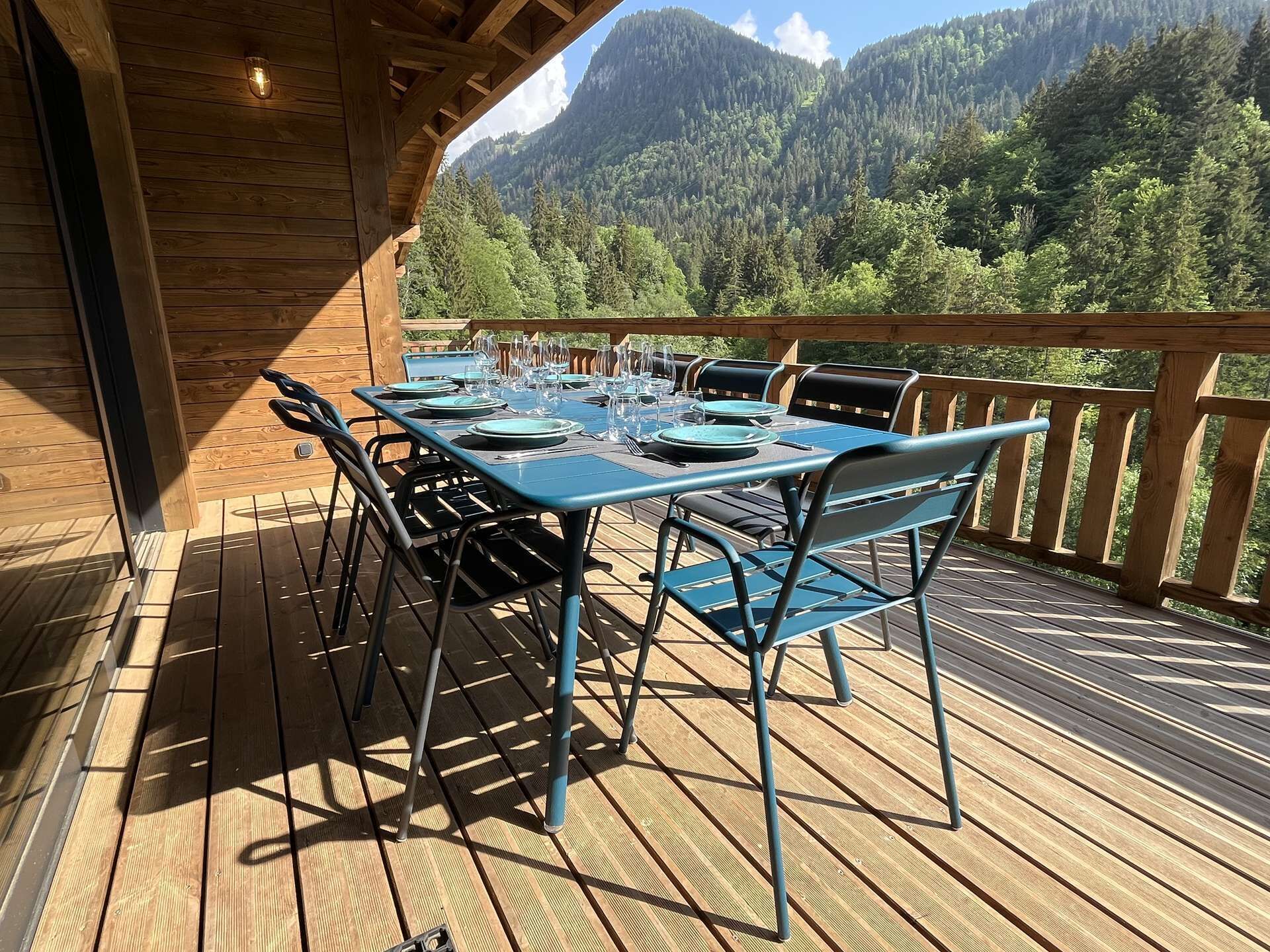 Eine Holzterrasse mit einem für das Essen gedeckten Tisch, mit Blick auf eine gebirgige Landschaft.