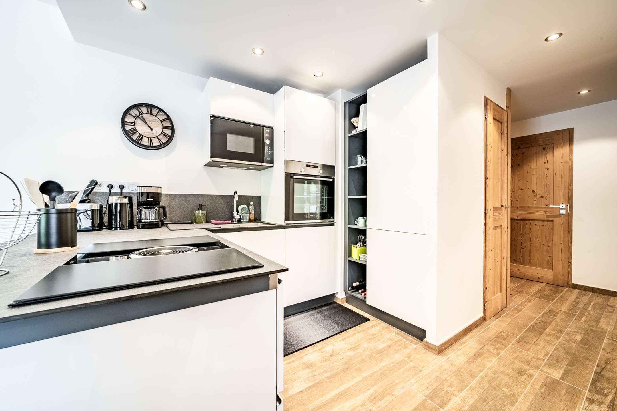 A modern kitchen with white cabinets, a microwave, an oven, and a clock on the wall.
