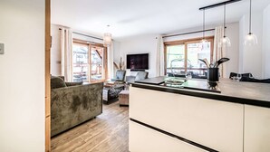 A modern kitchen with a wooden countertop, a dining area with a sofa and chairs, and large windows with curtains.