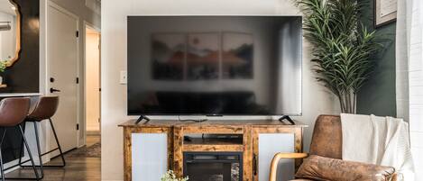 A living room with a large flat-screen TV, a fireplace, a sofa, and a dining area with chairs.
