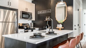 A modern kitchen with stainless steel appliances, a central island with seating, and a decorative mirror. - Greenbelt Balcony 2BR | Hot Tub, Steps to Downtown (Boise)