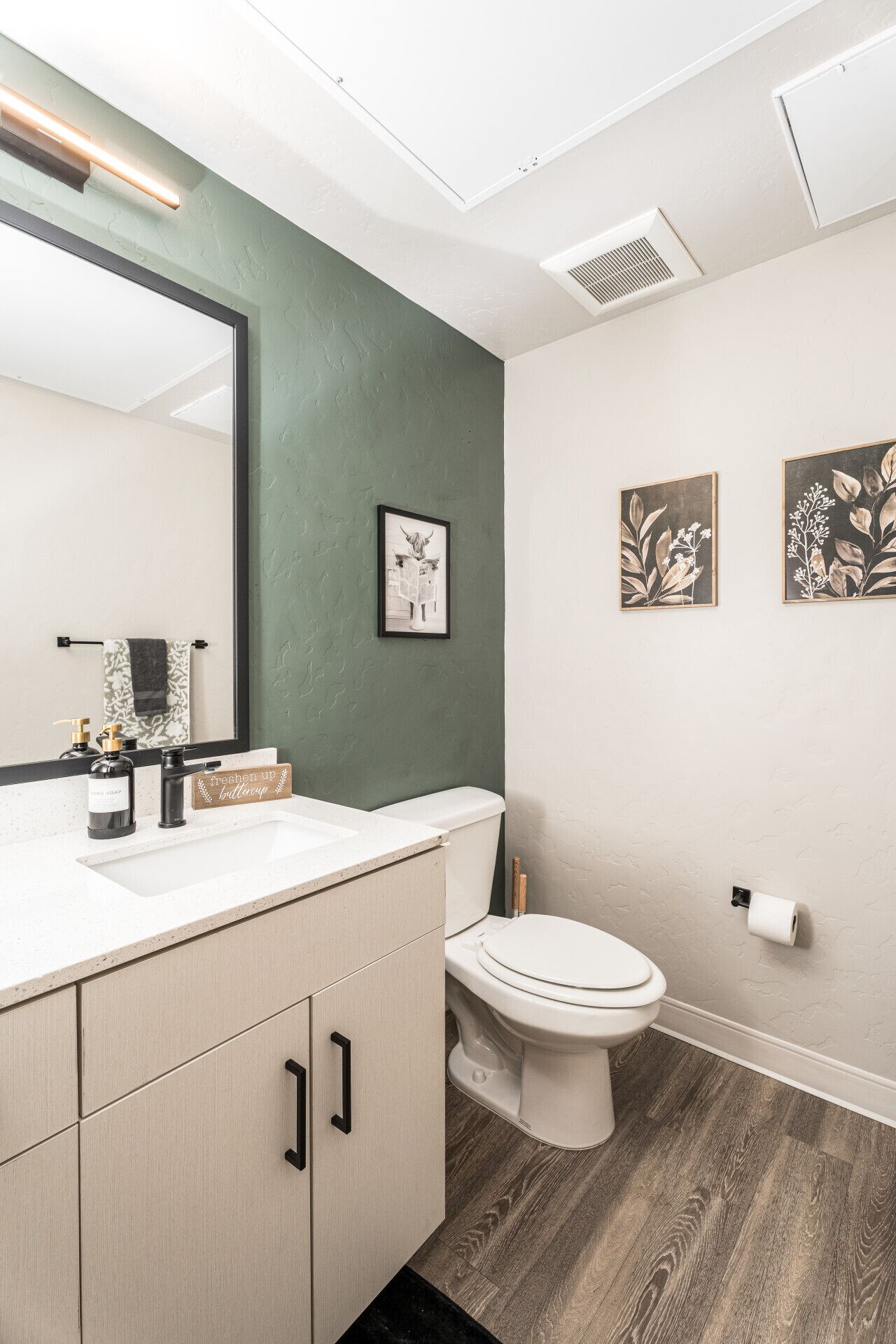 A modern bathroom with a white sink, a mirror, a toilet, and a green accent wall.