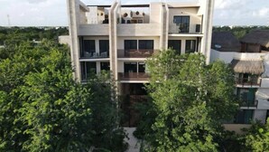 Un edificio moderno de varios pisos con balcones y ventanas amplias, rodeado de abundante vegetación.