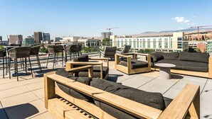 Una terraza en la azotea con muebles de madera, incluyendo sofás y sillones, y vistas de la ciudad.