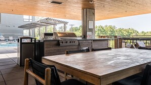Eine Terrassenausstattung im Freien mit Holztisch, Stühlen, einem Grill und einem Pool im Hintergrund.