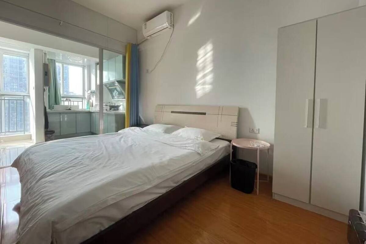 A modern bedroom with a large bed, a bedside table, a wardrobe, and a window with a view.