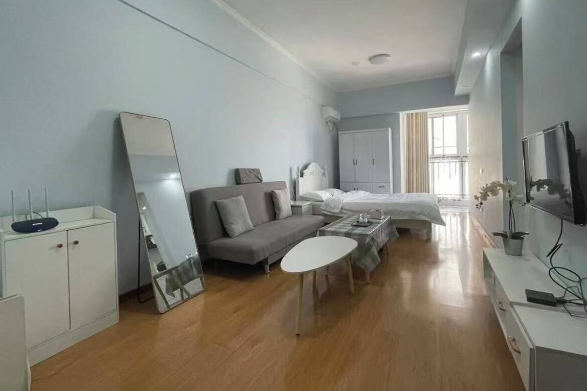 A modern hotel room with a sofa, a small table, a bed, a TV, and a wardrobe.