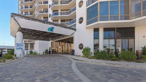 Une entrée d’hôtel moderne, dotée d’une allée couverte, de grandes fenêtres et d’un espace paysager.