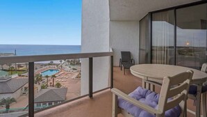 Un balcon donnant sur une piscine et des immeubles, une table ronde avec des chaises et un fauteuil rembourré.