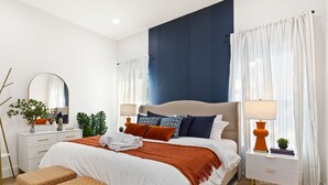Une chambre à coucher moderne avec un grand lit, une table de chevet avec une lampe, une commode et un miroir.