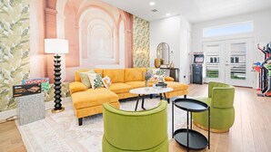 Un salon moderne avec un canapé jaune, des fauteuils verts, une table basse et une fresque murale représentant des arches.