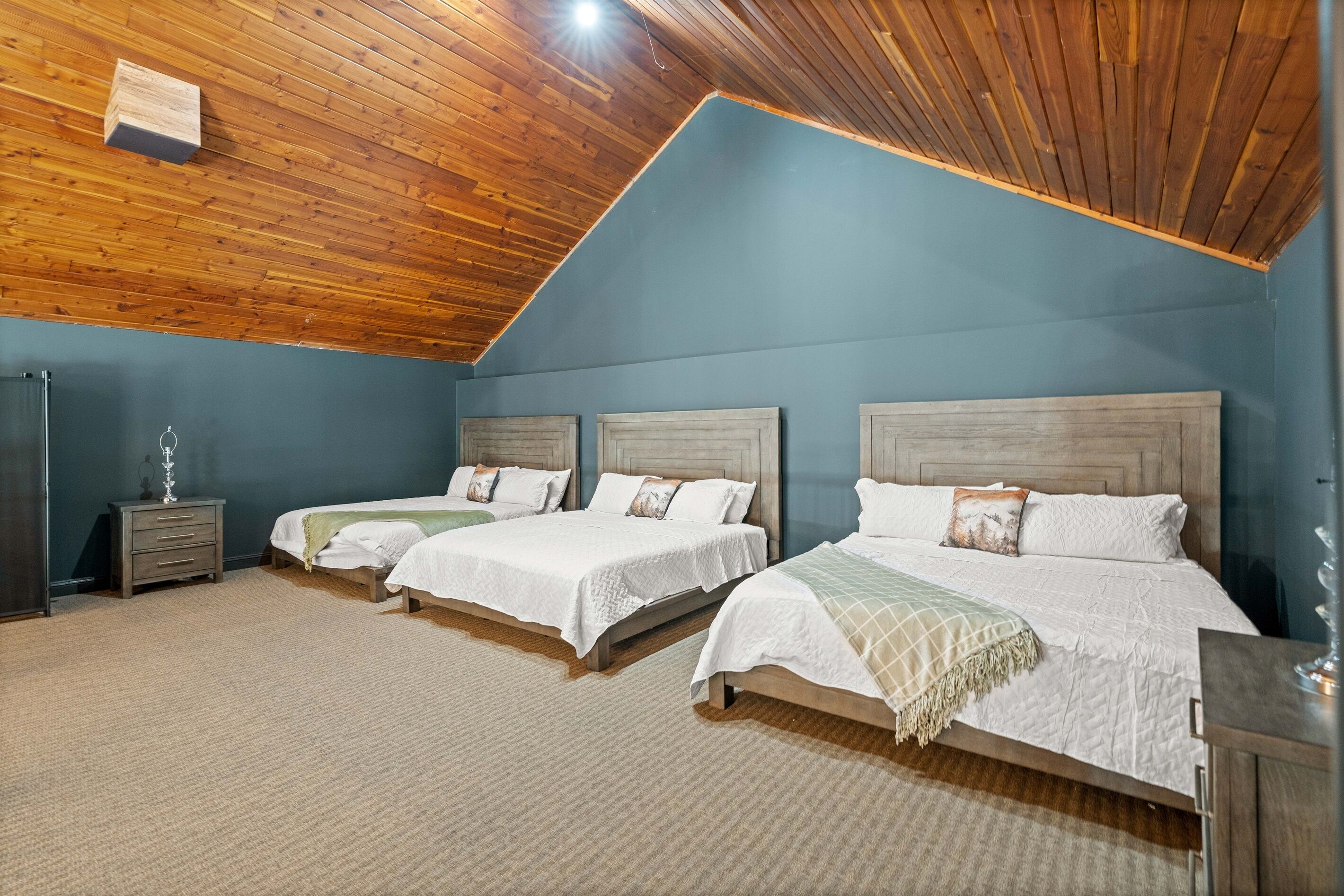 A bedroom with three beds, wooden ceiling, and a blue wall.