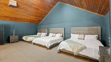 A bedroom with three beds, wooden ceiling, and a blue wall.
