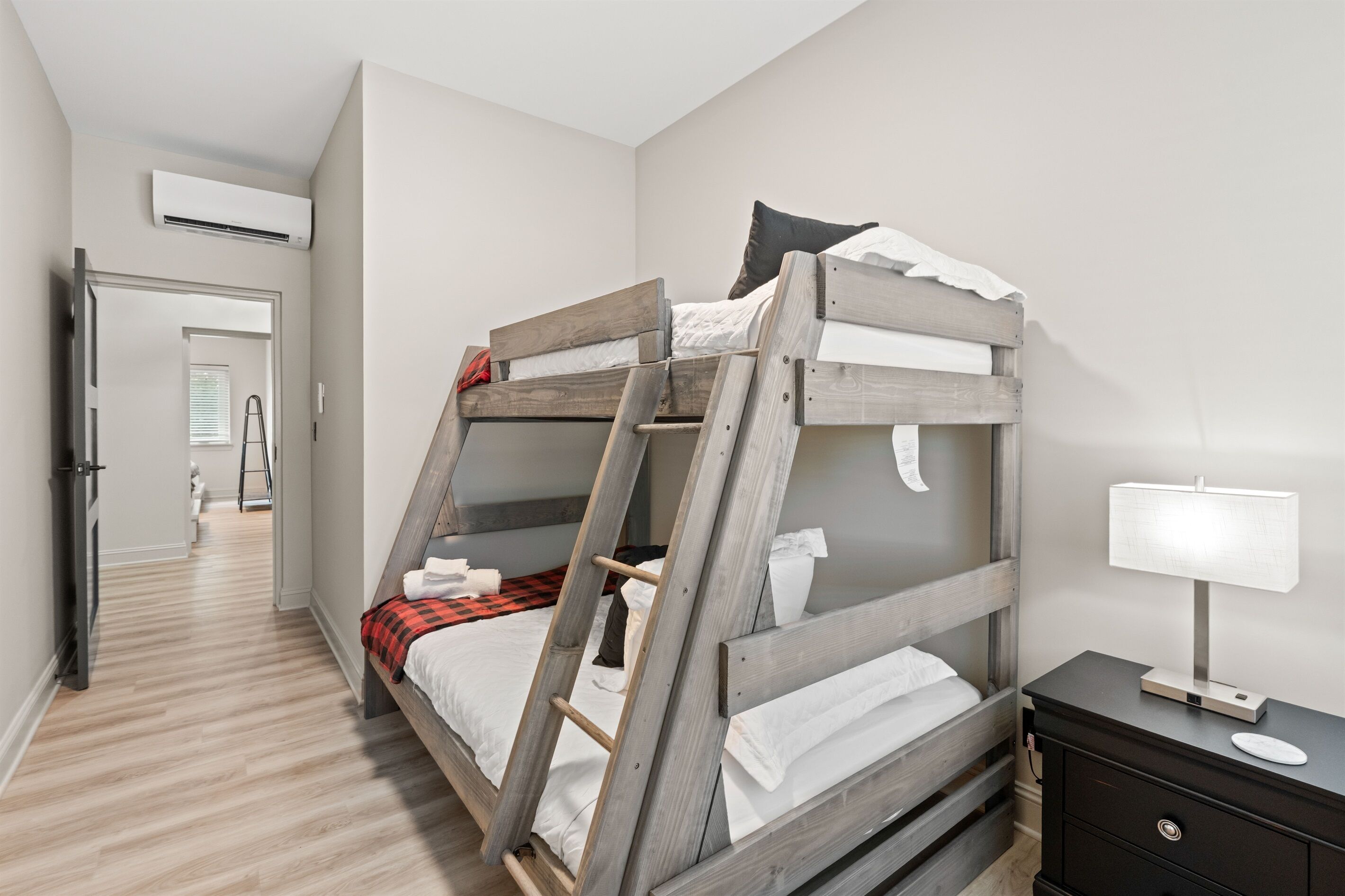 A bunk bed with a ladder, a bedside table with a lamp, and a door leading to a bathroom.
