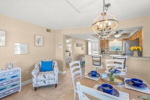 Una cucina moderna con un lampadario, zona pranzo con stoviglie blu e un soggiorno con divano a fantasia.
