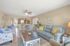 A spacious living room with a grey sofa, a wooden coffee table, and a dining area with a chandelier.