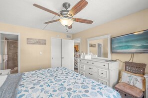 A bedroom with a bed, a ceiling fan, a dresser, a chair, and a television on the wall. - Modern 2BR | Pool View | Steps to Crescent Beach (Sarasota)