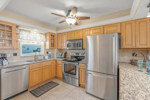 A kitchen with wooden cabinets, stainless steel appliances, a microwave, a stove, and a refrigerator. - Modern 2BR | Pool View | Steps to Crescent Beach (Sarasota)