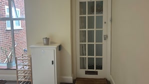 A white door with a number 5, a small potted plant on a white cabinet, and a wooden rack beside a window. - Homely flat in Surrey, Sleeps 3, family friendly (Walton-on-Thames)