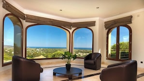 A spacious room with large arched windows offering a view of the landscape. There are two leather armchairs and a small round table with a potted plant. - 8 bedroom luxury villa + sea, golf course and mountain views (Sotogrande)