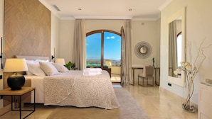 A hotel room with a large bed, a desk, a chair, a view of the sea, and a balcony. - 8 bedroom luxury villa + sea, golf course and mountain views (Sotogrande)