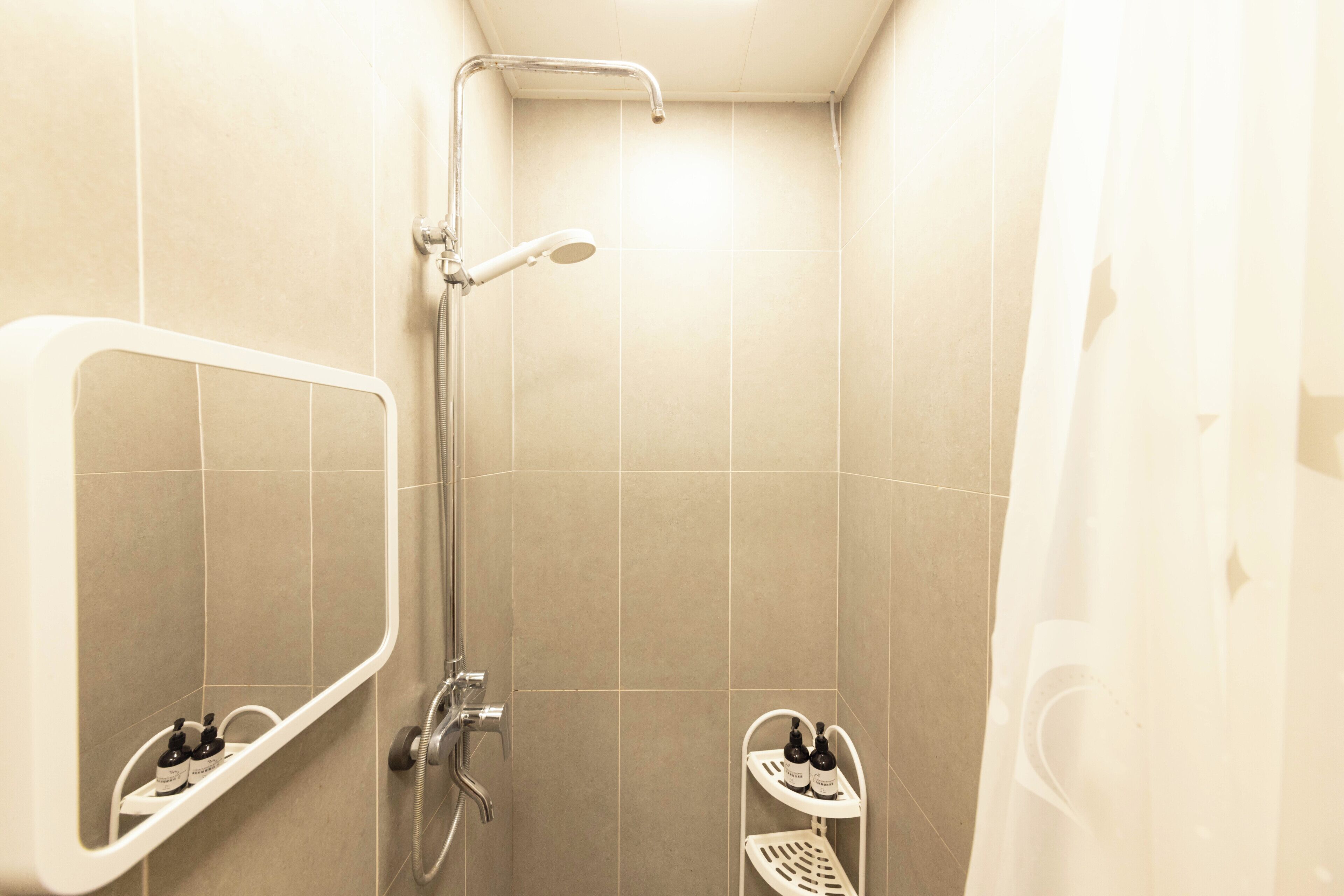 Un baño pequeño con ducha, un espejo y dos repisas con botellas.