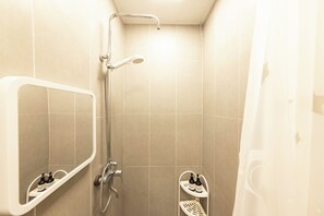 A small bathroom with a shower, a mirror, and two shelves with bottles.