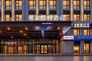 A hotel entrance with a modern facade, illuminated signage, and a glass entrance.
