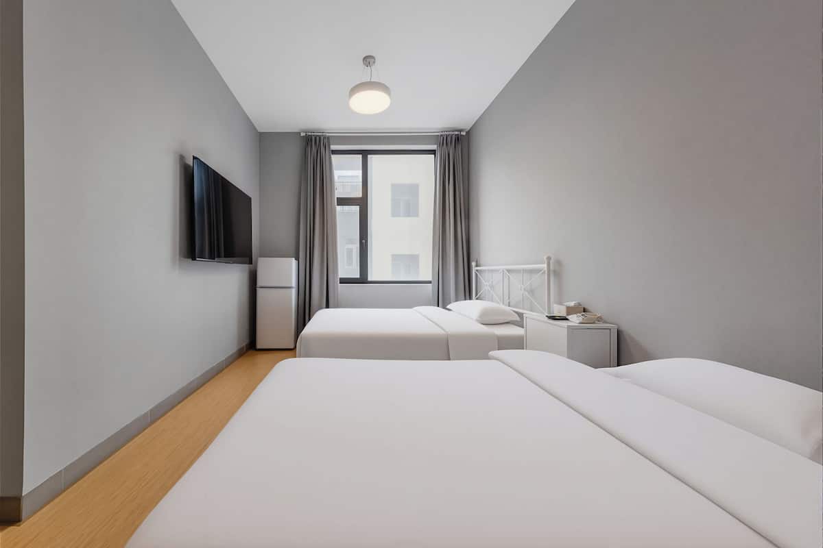 A modern hotel room with a large bed, a TV, a bedside table, and a window with curtains.