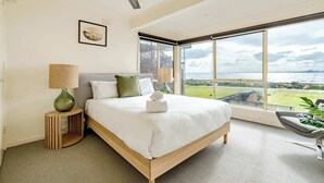A bedroom with a large bed, a ceiling fan, a view of the sea, and a window with a view of the sea.