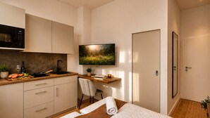 Una camera da letto moderna con un letto, una scrivania, una TV e un angolo cottura.