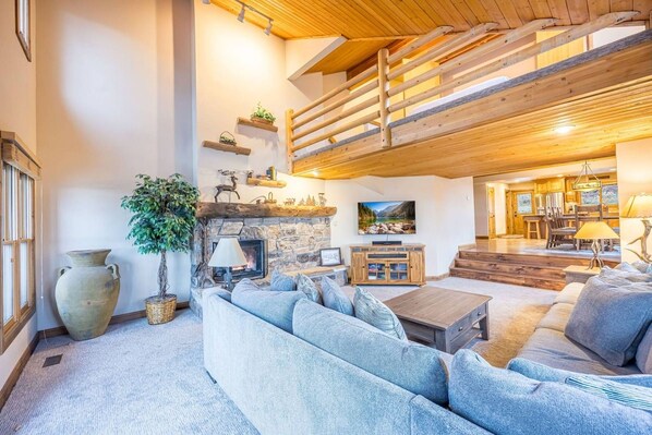 Una sala de estar acogedora con chimenea de piedra, un sofá grande y un techo de madera.