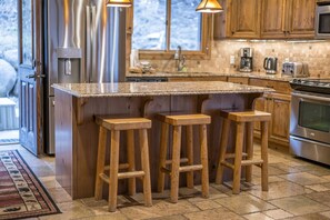 Una cocina con encimera de granito, taburetes de madera, electrodomésticos de acero inoxidable y armarios de madera.
