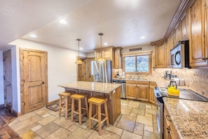A kitchen with wooden cabinets, a granite countertop, a stainless steel refrigerator, and a yellow kettle.