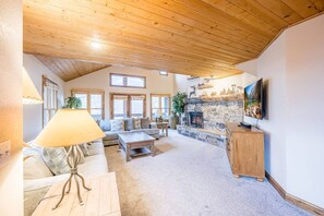 A cozy living room with a stone fireplace, wooden ceiling, and a large window. - Group of 40? 4 Side-by-Side Homes, Walk to Park City Mountain & Main, Hot Tubs (Park City)