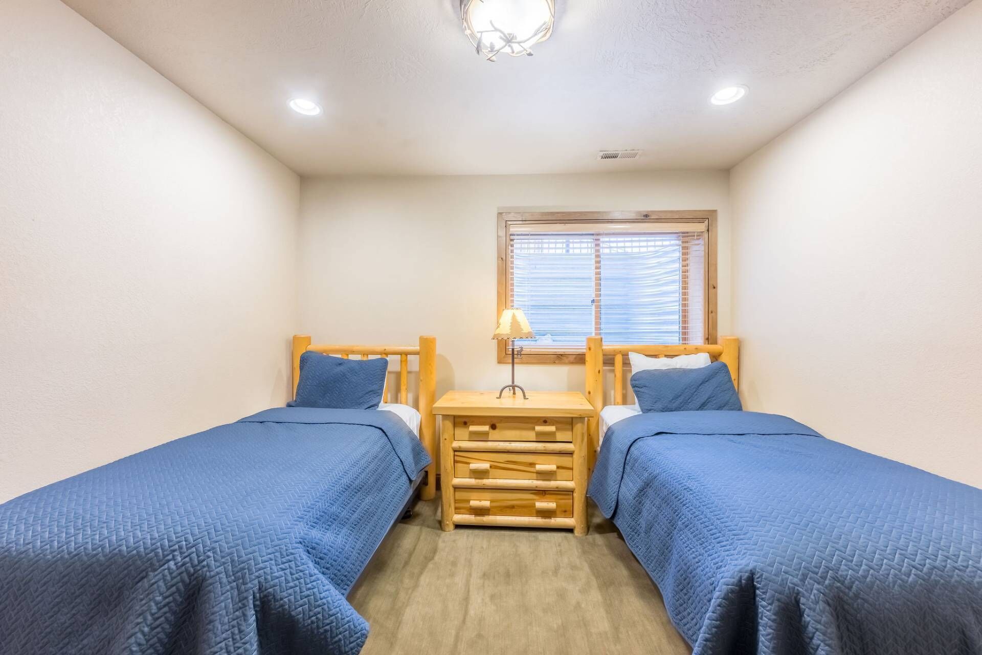 A small, cozy room with two single beds, a nightstand with a lamp, and a window with blinds.