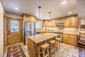 A spacious kitchen with wooden cabinets, a granite countertop, stainless steel appliances, and a large island with bar stools.