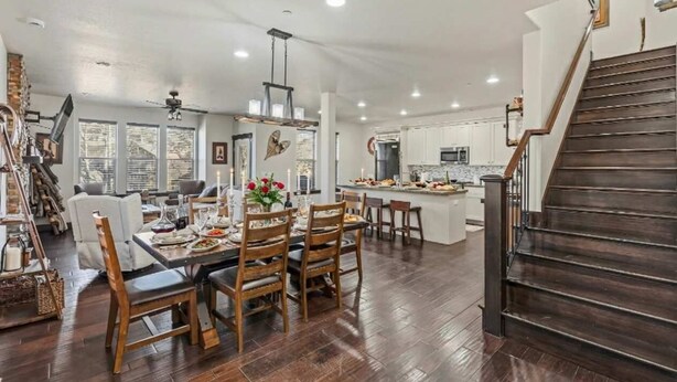 A spacious dining area with a wooden table and chairs, a kitchen with a central island, and a dark wooden staircase. - Aspen Crest Condo, 4BR, Deer Valley, hot tub (Kamas)