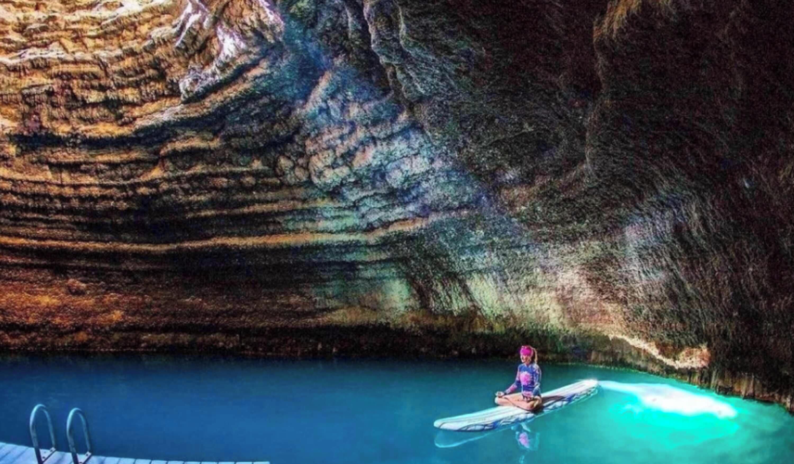 Una persona haciendo kayak en una piscina con un fondo que parece una cueva.