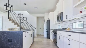 A modern kitchen with a central island, stainless steel appliances, and a staircase with black railings.