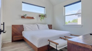 A bedroom with a bed, bedside tables, a desk, and two windows.