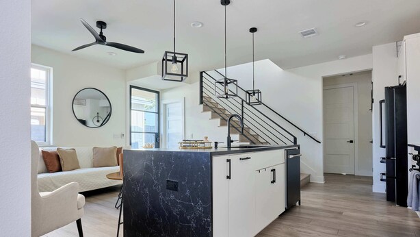 A modern kitchen with a central island, a dining area with a sofa, and a staircase leading to another level.