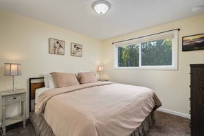 A bedroom with a bed, two bedside tables with lamps, a window with a view of trees, and two wall-mounted pictures. - Alpine Getaway w/ Hot Tub, Firepit & Stunning Views, Pet Friendly, Near Mt. Hood Slopes (Welches)