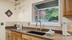 Una cocina con ventana, pileta, cafetera y armarios de madera.