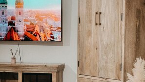 A modern living room with a wooden cabinet, a mounted TV displaying a cityscape, and a fur rug. - Exclusive whirlpool apartment & mountain view (Steinhöring)