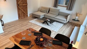 A dining area with a wooden table, black chairs, and a candle centerpiece. A sofa and a window with curtains are in the background. - Exclusive whirlpool apartment & mountain view (Steinhöring)