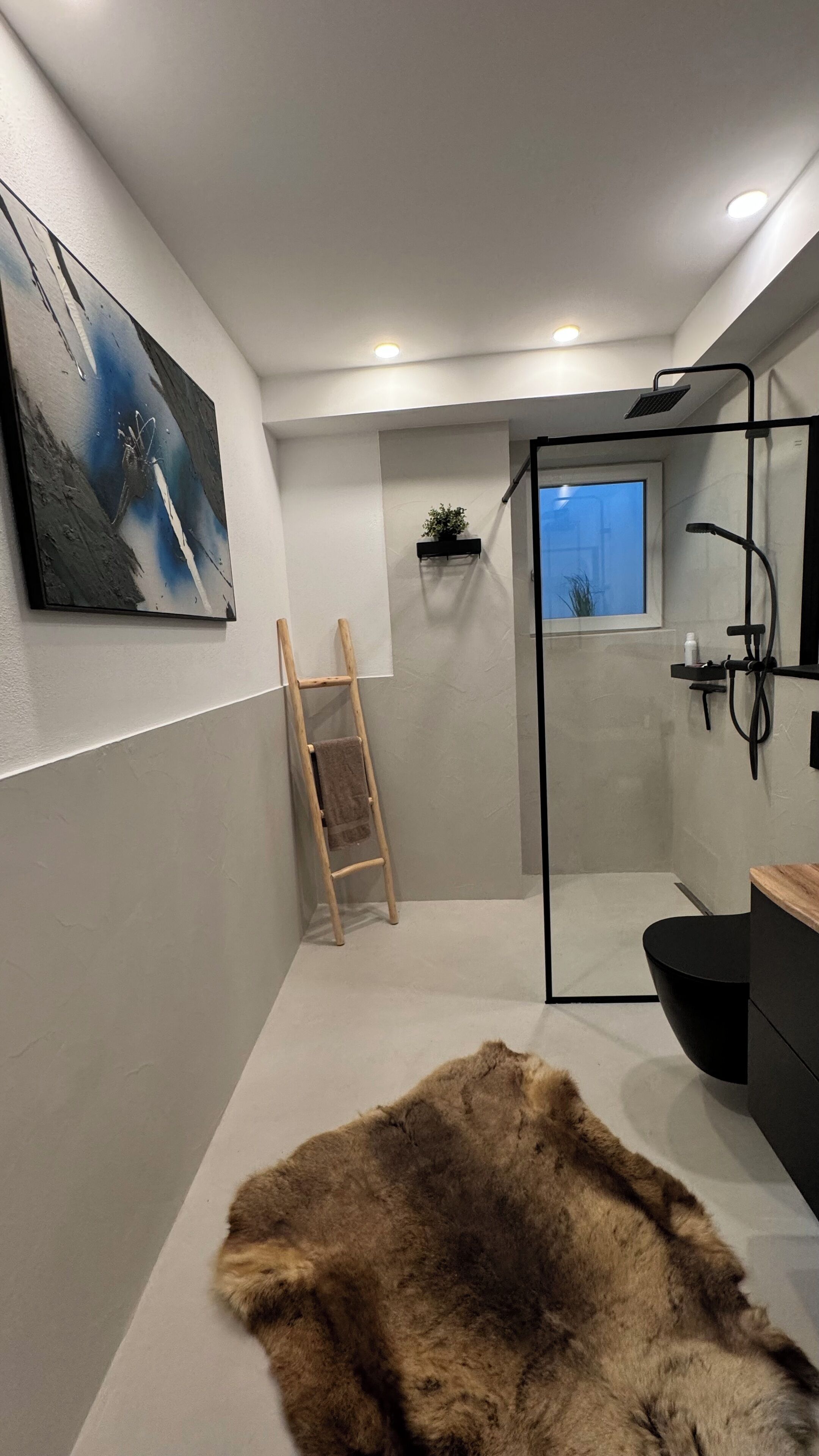 Ein modernes Badezimmer mit Duschkabine aus Glas, einer Holzleiter, einem Fellteppich und einem Bild an der Wand.