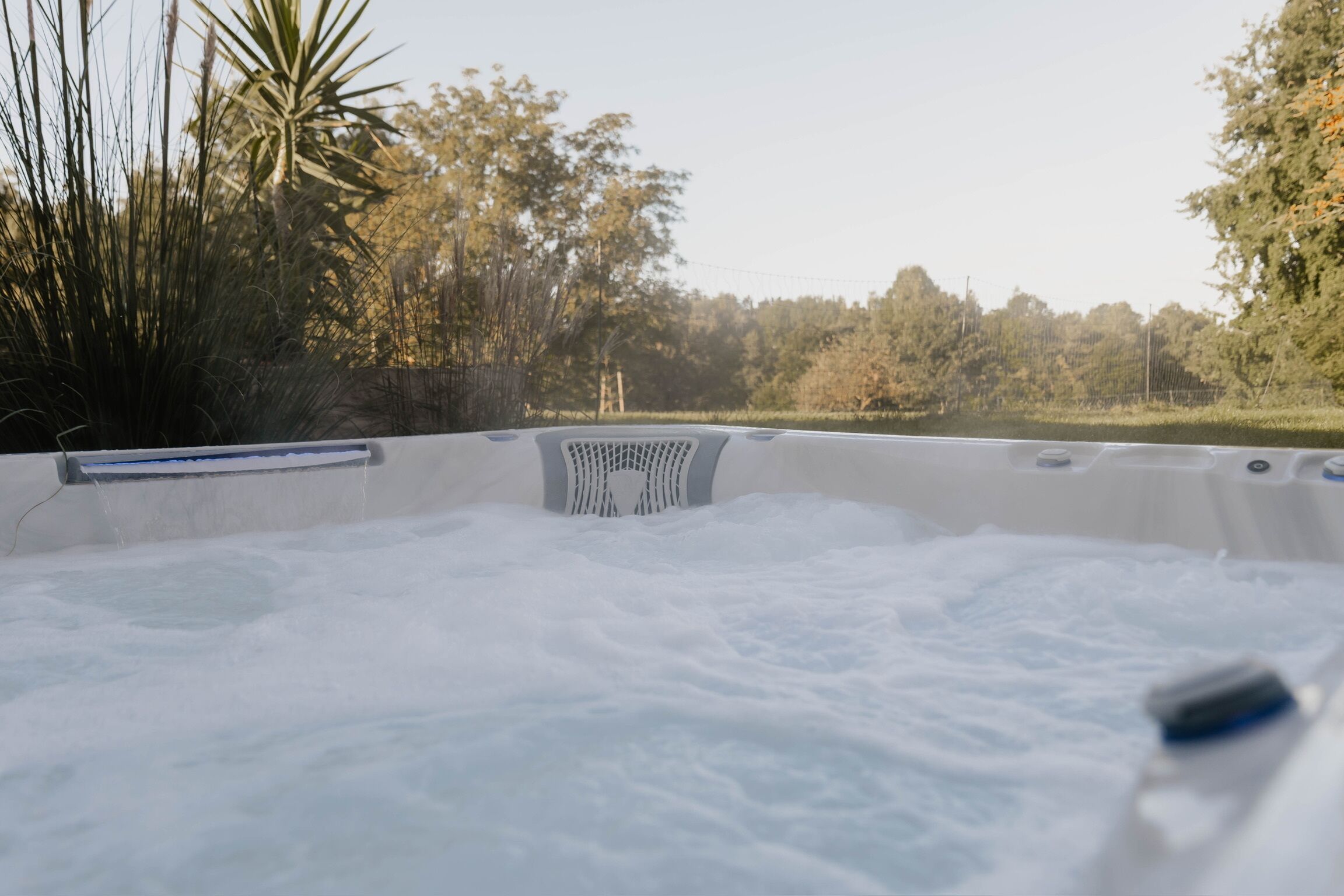 Een hottub omgeven door bomen en een hek.
