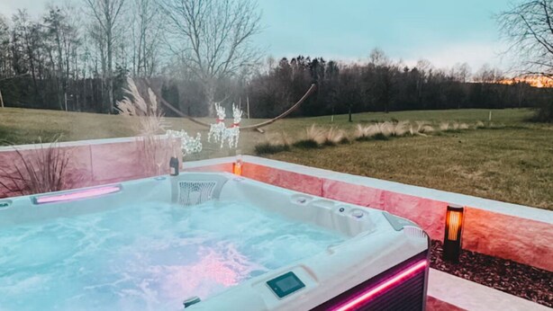 A hot tub on a wooden deck with a view of a grassy field and trees in the background. - Exclusive whirlpool apartment & mountain view (Steinhöring)
