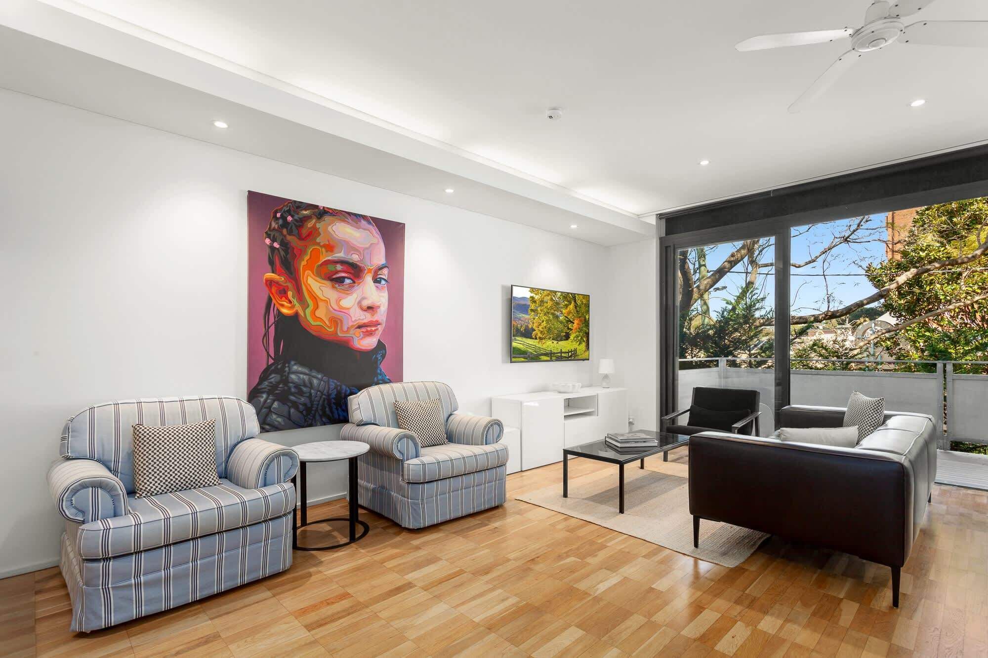 A modern living room with a large window, a ceiling fan, and two sofas.